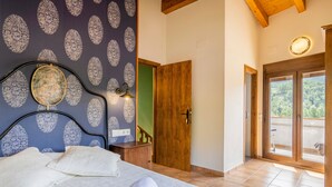 Une chambre avec un lit, un miroir, un mur orné d’un motif floral, une porte en bois et une vue à travers une porte vitrée.