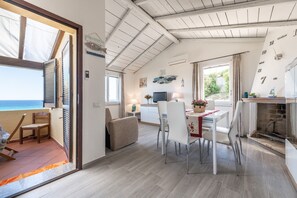 A room with a view of the sea, a dining area with chairs and a table, and a fireplace.