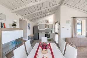 A modern kitchen with white cabinets, a dining table with a red runner, and a view of the sea through a window.