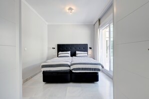 A modern bedroom with a large bed, a headboard, and a window providing natural light.