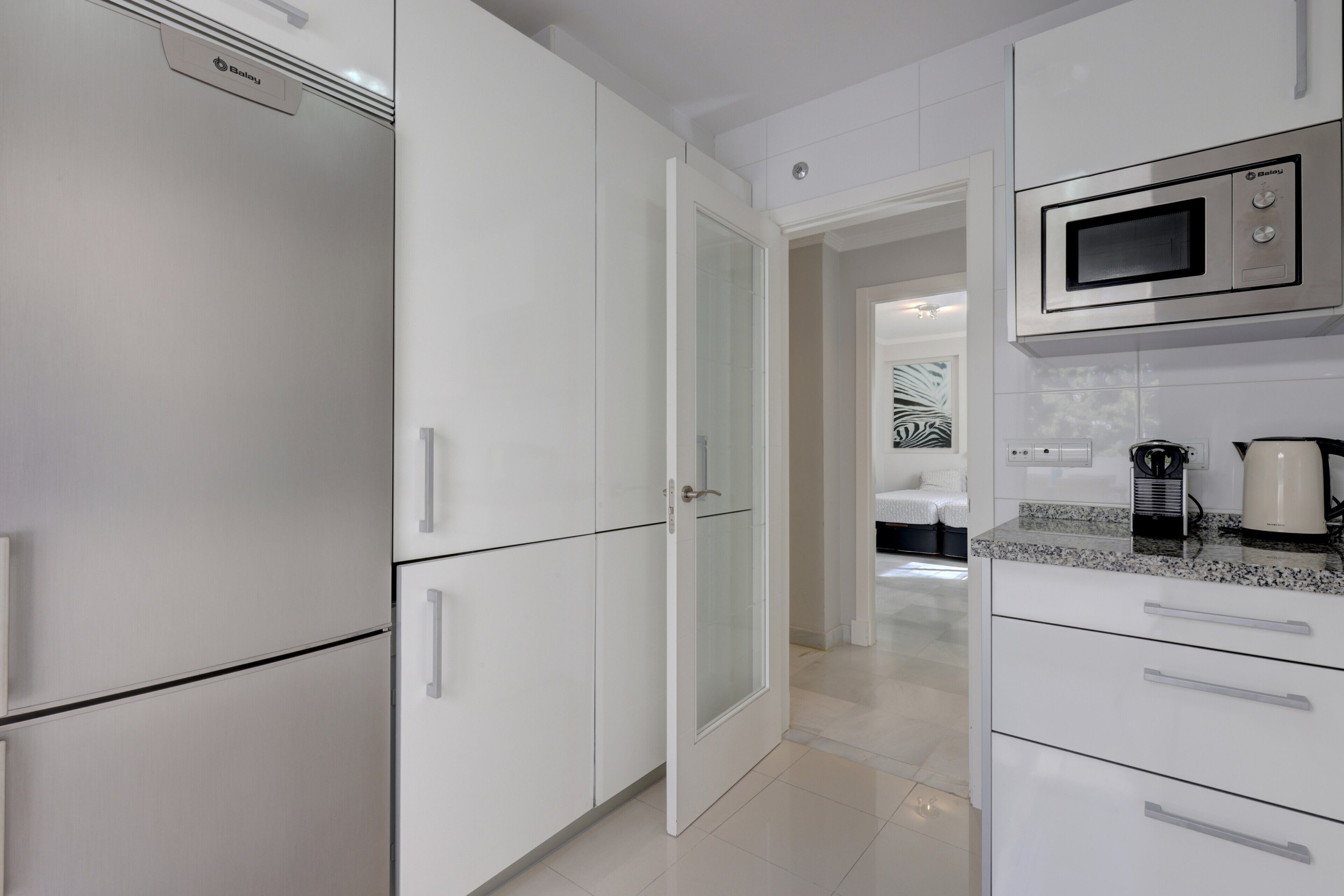 A modern kitchen with white cabinetry, a microwave, and a coffee maker.