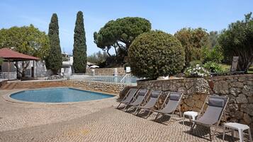 A pool area with lounge chairs, a stone wall, and a large tree.