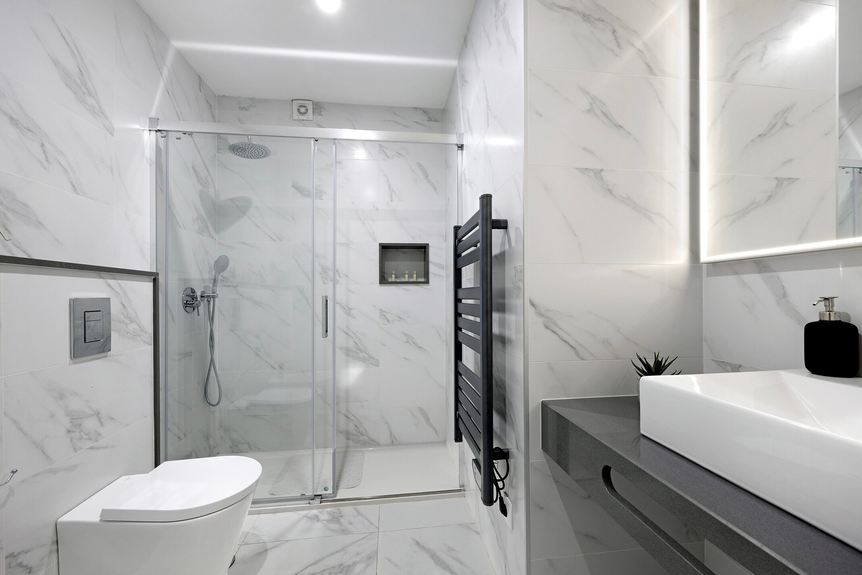 A modern bathroom with a glass-enclosed shower, a white toilet, a black towel rack, and a large mirror above the sink.