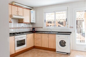 Una cucina compatta con piano cottura, forno, lavello e lavatrice, pensili in legno e una finestra con vista.