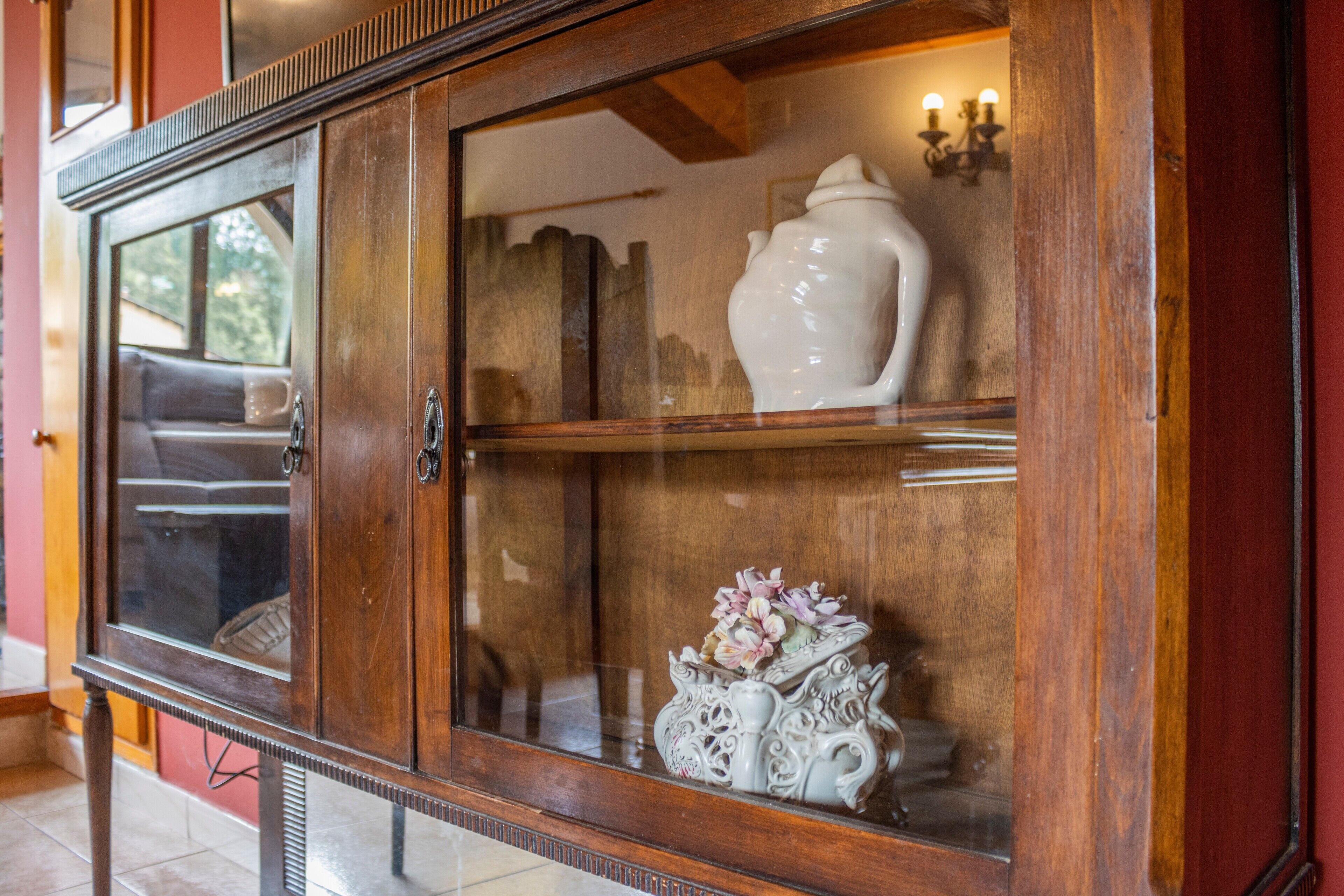 A wooden cabinet with glass doors, a white ceramic pitcher, and a decorative vase with flowers.