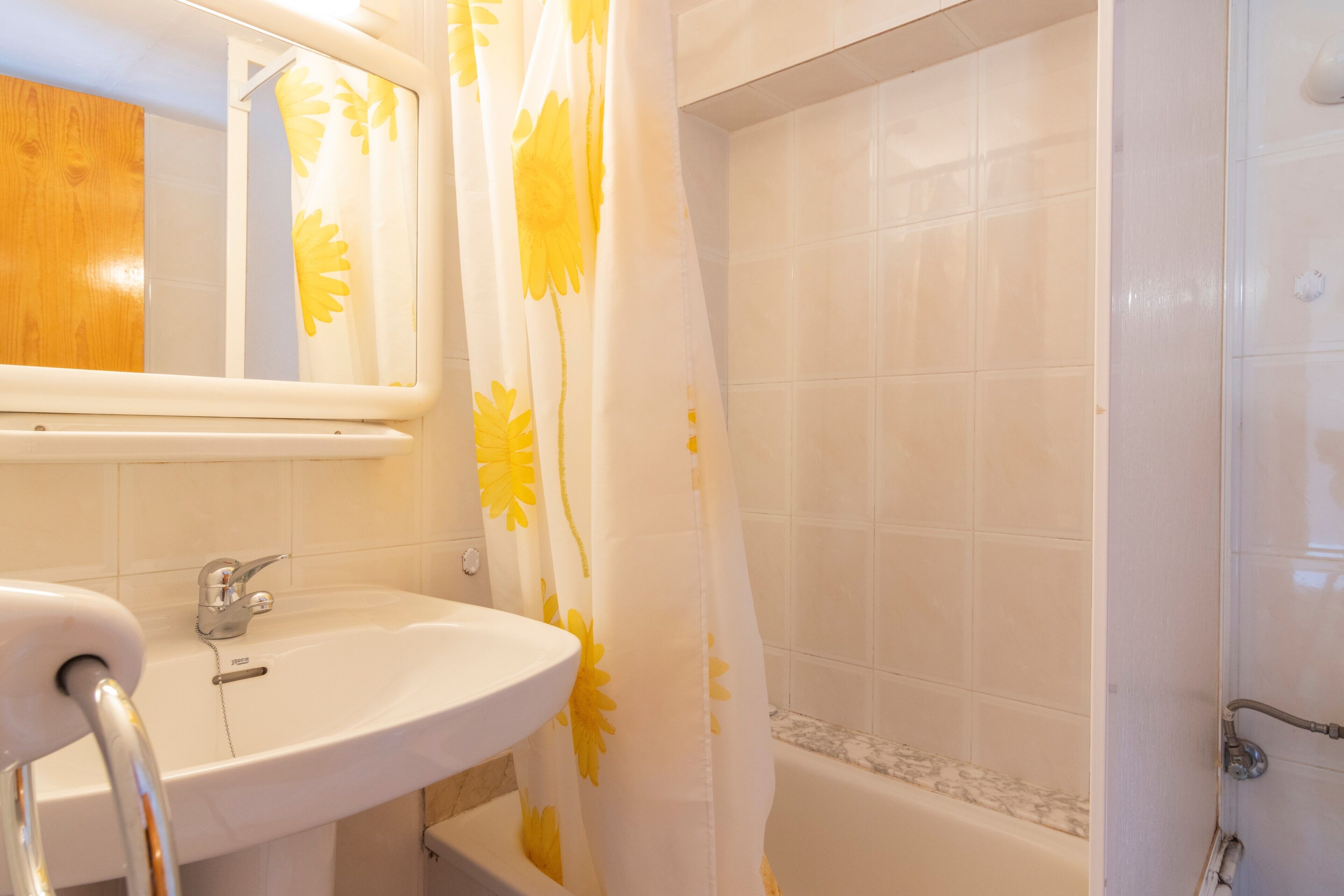 A bathroom with a white sink, a mirror, a shower curtain with yellow floral patterns, and a bathtub.