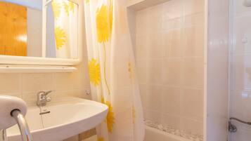 A bathroom with a white sink, a mirror, a shower curtain with yellow floral patterns, and a bathtub.
