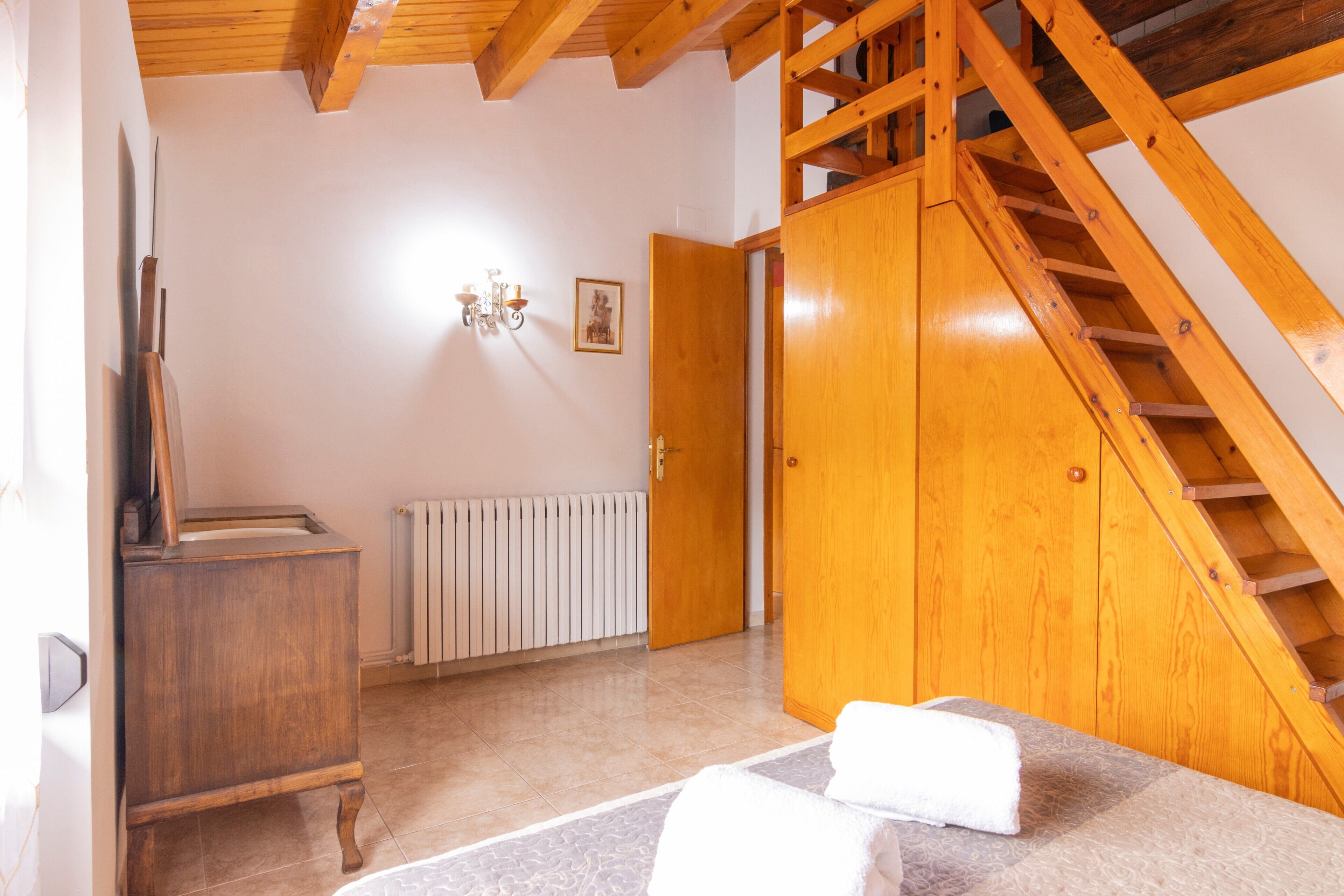 Una habitación con una escalera de madera, un radiador, un armario de madera y una cama con una toalla blanca.