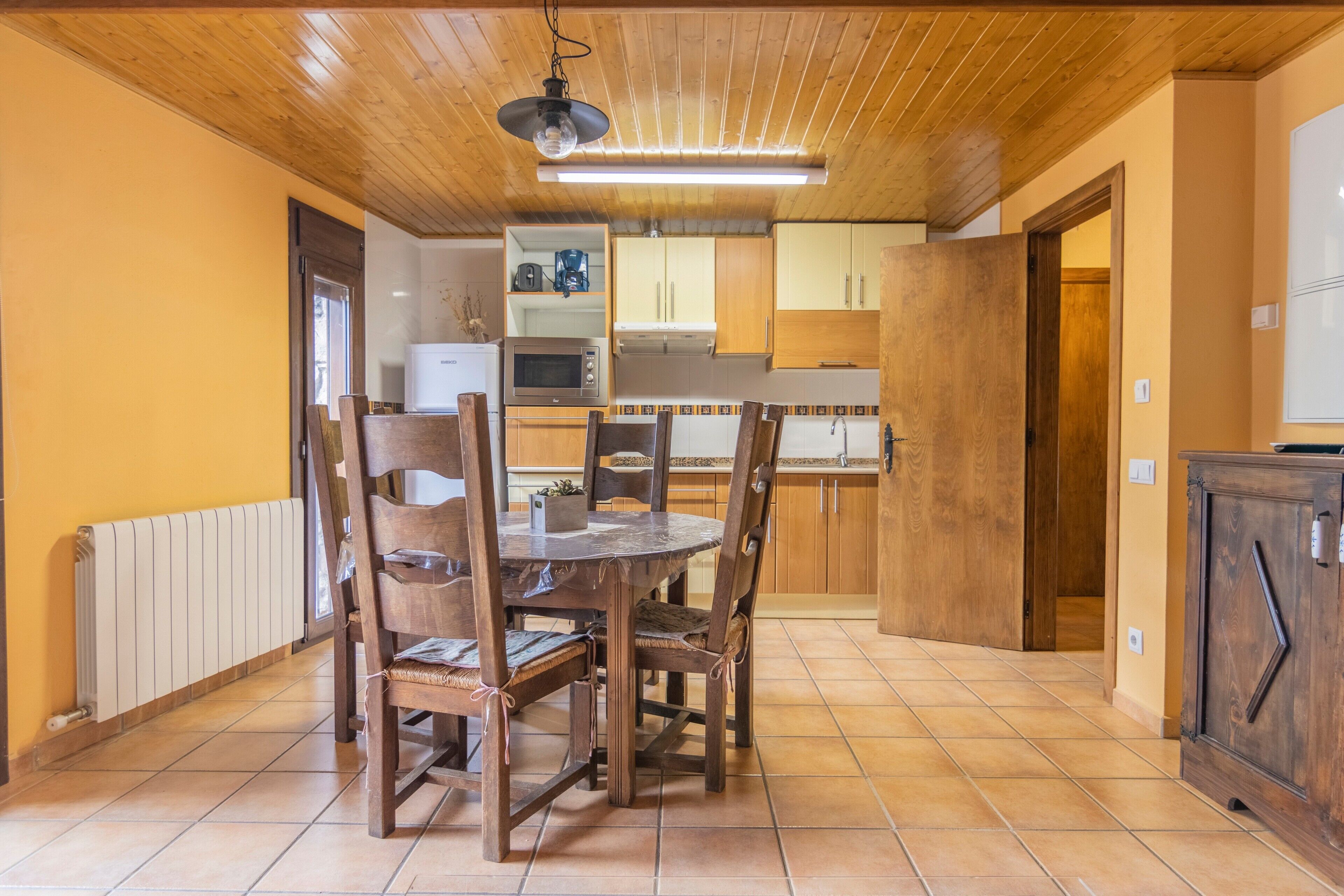 Un coin repas avec une table et des chaises en bois, une cuisine à l’arrière-plan et un plafond en bois.