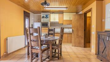 Un coin repas avec une table et des chaises en bois, une cuisine à l’arrière-plan et un plafond en bois.