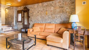 A living room with a stone wall, a wooden ceiling, a sofa, a coffee table, a lamp, and a chair.