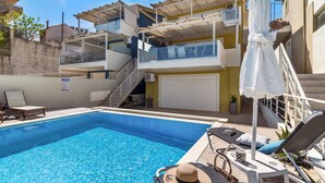 Une piscine avec des chaises longues, un parasol et un escalier menant à un balcon.