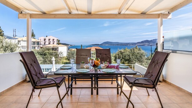 Un espace de restauration extérieur abrité, avec une table dressée pour deux personnes, offrant une vue panoramique sur la mer et les collines.