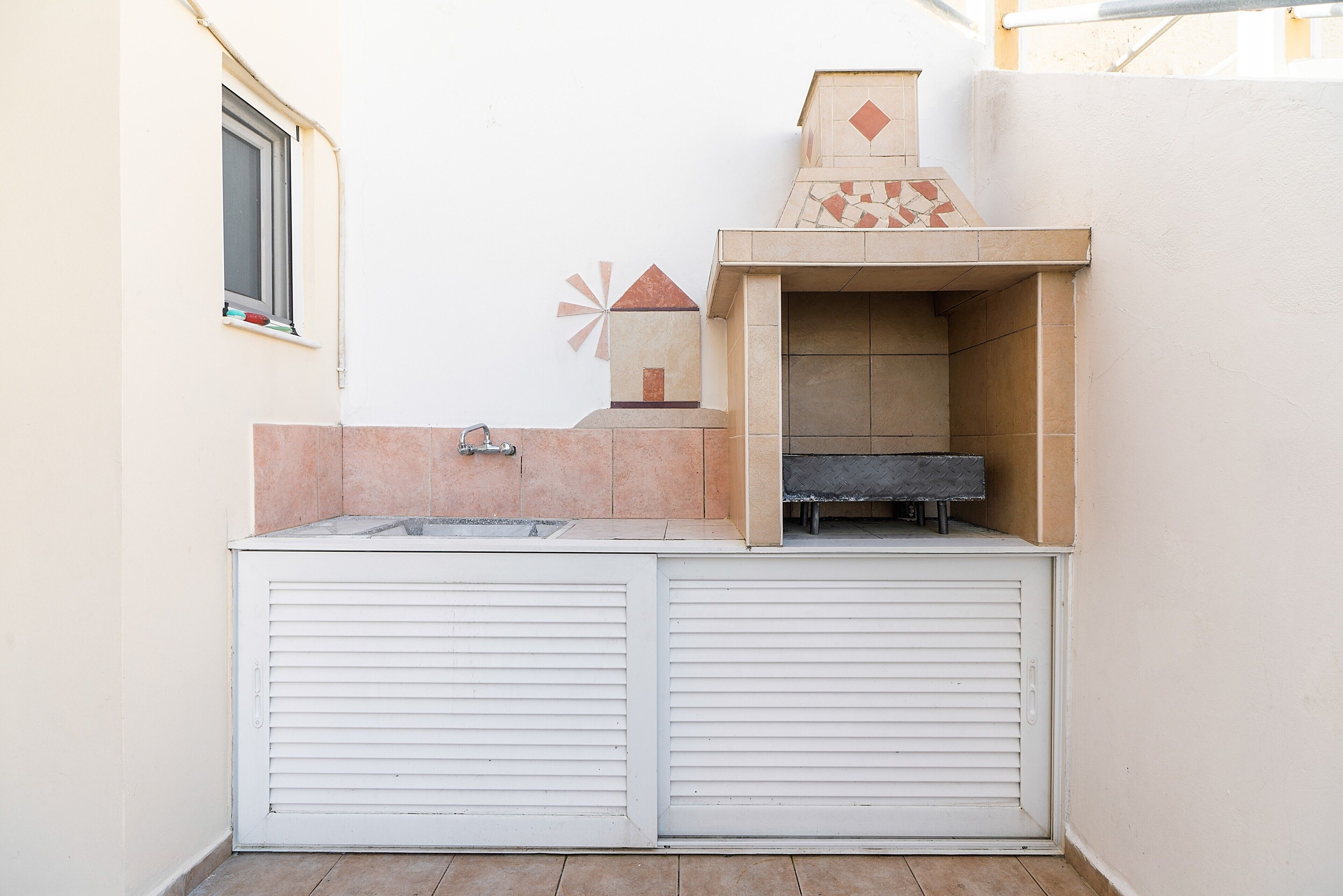 Una cocina exterior compacta con una parrilla integrada, un ventanal y un salpicadero de azulejos.