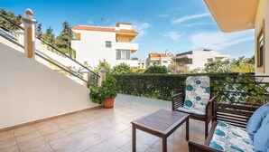 A balcony with a wooden table and chairs, a potted plant, and a view of neighboring buildings. - Apartment 'Rafaela's House' with Shared Pool, Wi-Fi and Air Conditioning (Koskinou)