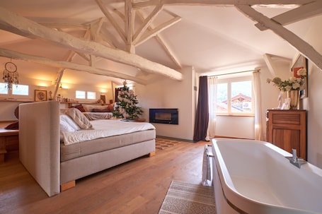 A bedroom with a bed, a wooden floor, a fireplace, and a large window.