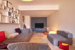 A modern living room with a sofa set, a flat-screen TV, a bookshelf, and a patterned rug.
