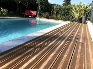 A wooden deck leading to a swimming pool with a red bench and potted plants.