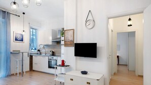 Een moderne keuken met witte kasten, een eethoek met een witte tafel en stoelen, een flatscreen-televisie aan de muur en een houten vloer.