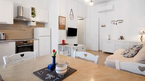 Een moderne keuken met witte kastjes, een roestvrijstalen afzuigkap en een eethoek met een houten tafel en stoelen.
