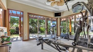 A gym with exercise equipment, large windows, and a view of greenery outside.