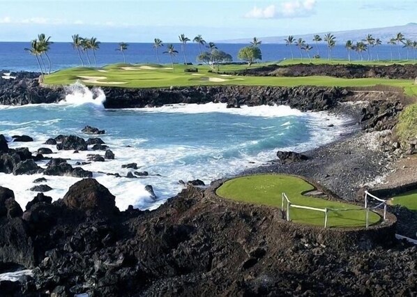 A coastal golf course with a rocky shoreline, a well-maintained green, and a clear view of the ocean.