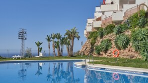 A swimming pool with a clear blue sky, palm trees, and a building with balconies. - Holiday Apartment "Paraíso Azul" with Sea View, Shared Pool (Summer) & A/C (Nerja)
