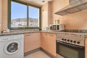A modern kitchen with a washing machine, microwave, oven, and a view of a hillside town.