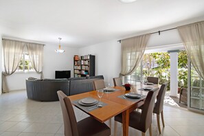 A modern living room with a dining table set for four, a sofa, and a bookshelf.