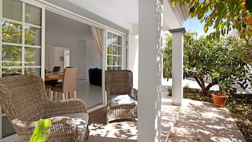 Eine Terrasse mit Korbmöbeln, eine Glastür zu einem Innenbereich und ein Blumentopf.