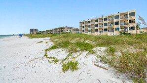 A beachfront hotel with multiple balconies, a sandy beach, and a clear sky.