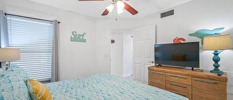 A bedroom with a bed, a ceiling fan, a TV, a dresser, and a wall with a 'Surf' sign.