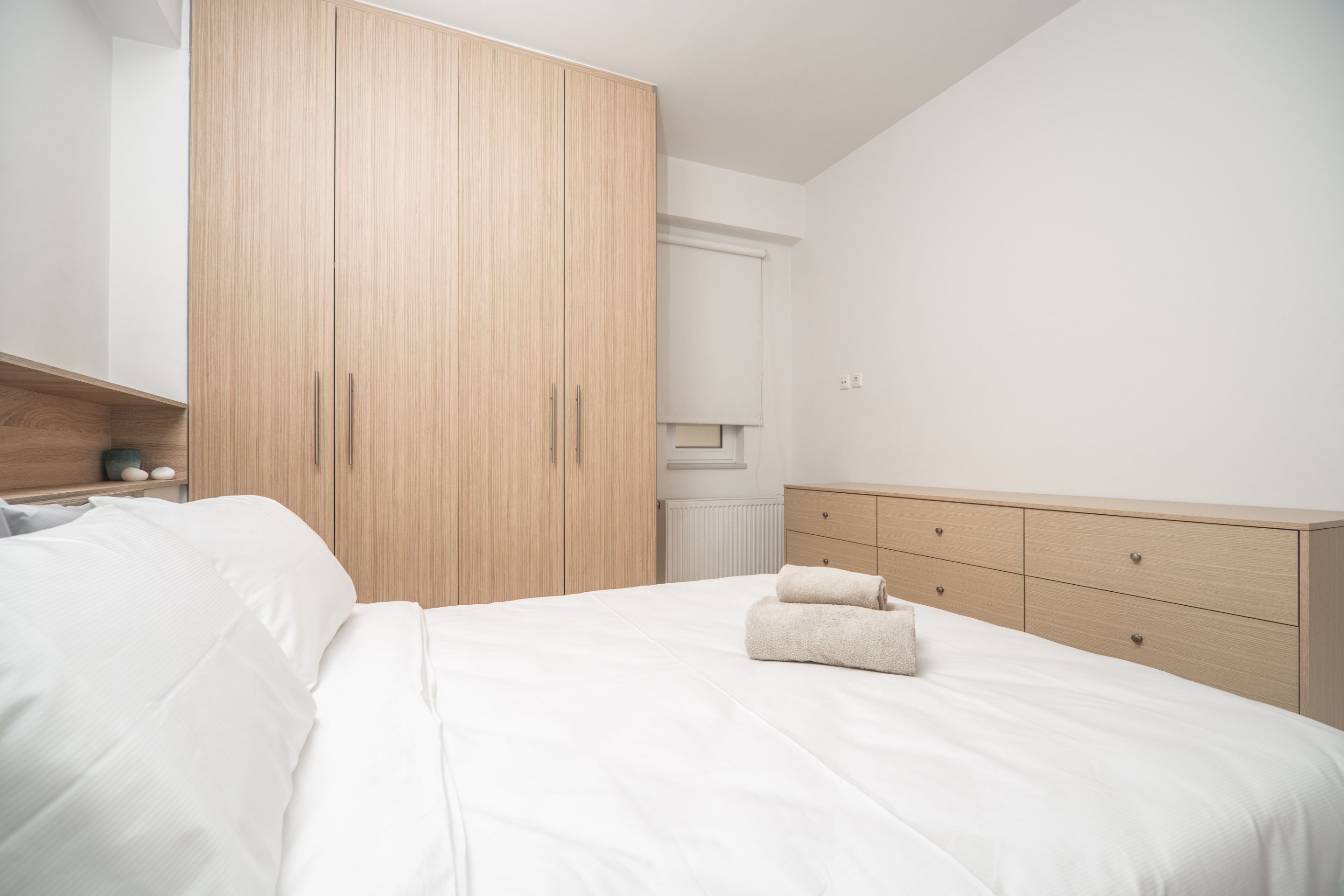 A bedroom with a large wardrobe, a bed with white linens, and a dresser with drawers.