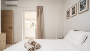A hotel room with a bed, a wooden wardrobe, an air conditioning unit, a door, and a window with curtains. - City beach apartment (Chania)