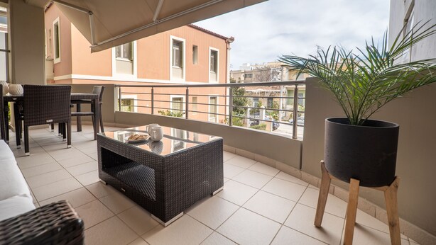 A balcony with wicker furniture, a glass-top table, and a potted plant. - City beach apartment (Chania)