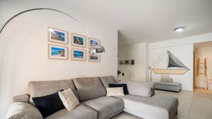 A living room with a large L-shaped sofa, a small grey sofa, and a wall-mounted sailboat decoration. - City beach apartment (Chania)