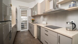A modern kitchen with stainless steel appliances, light wood cabinets, and a built-in oven. - City beach apartment (Chania)
