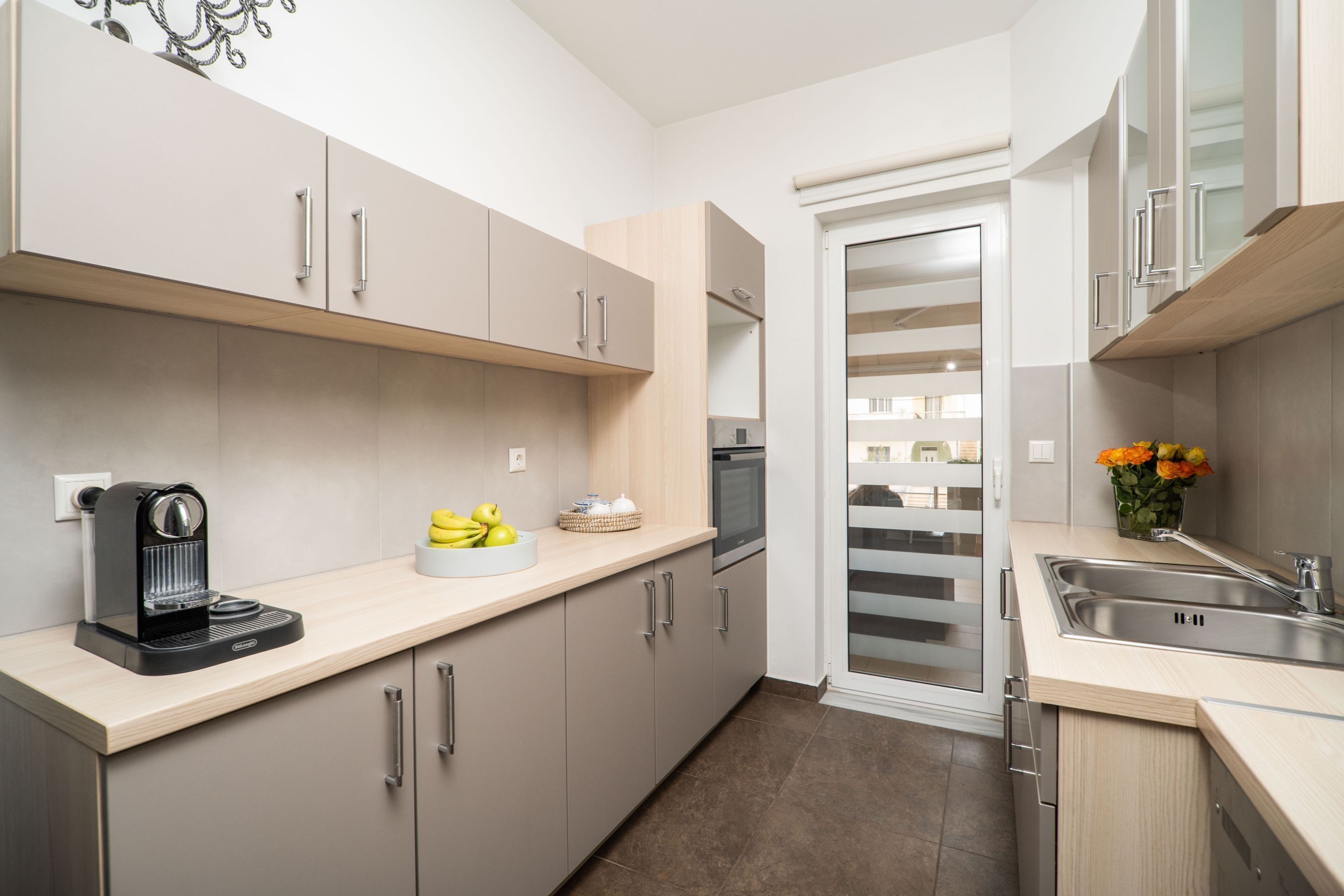 A modern kitchen with light wood cabinets, a built-in oven, a coffee maker, and a sink.