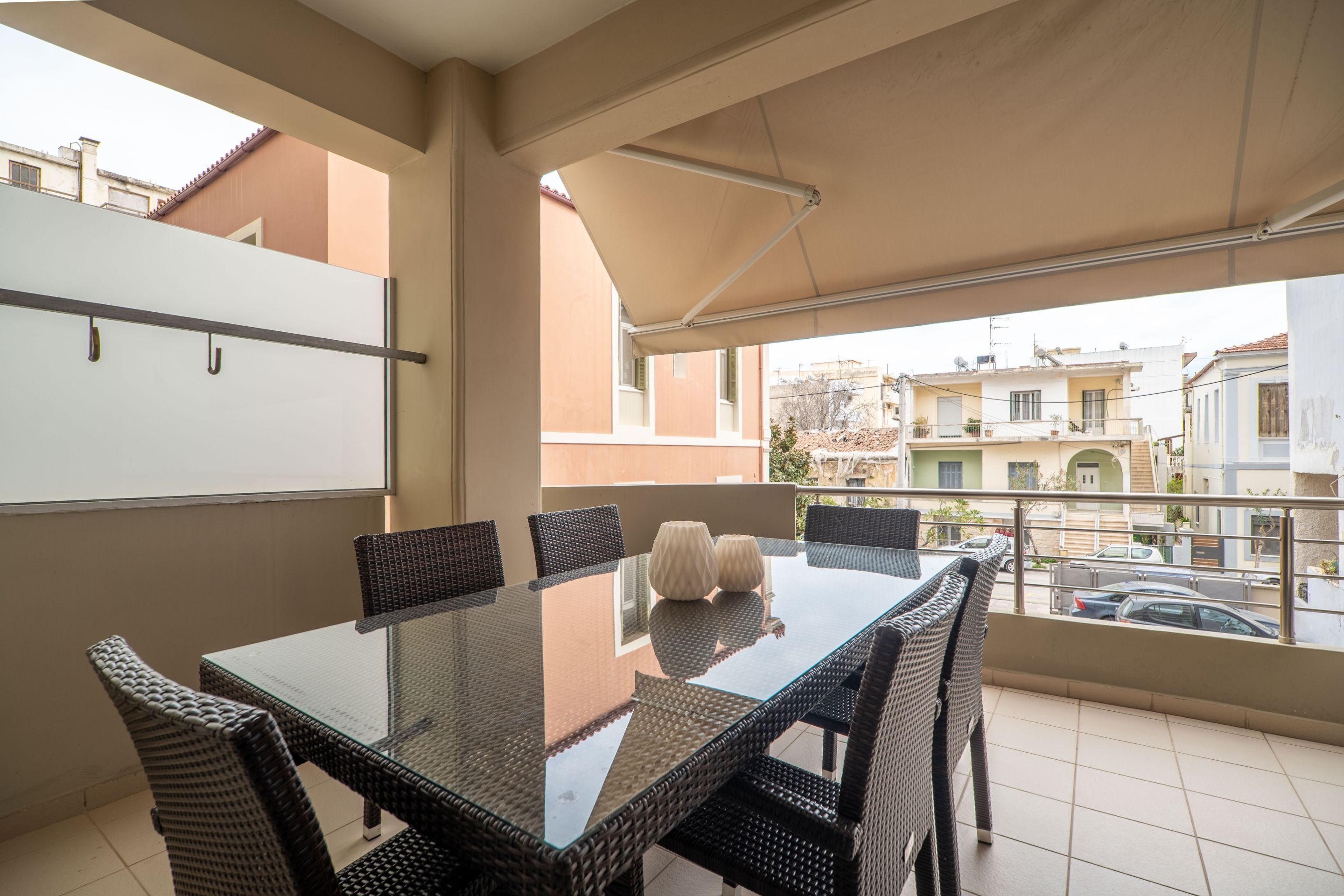 A balcony with a glass table and wicker chairs, overlooking a residential area.