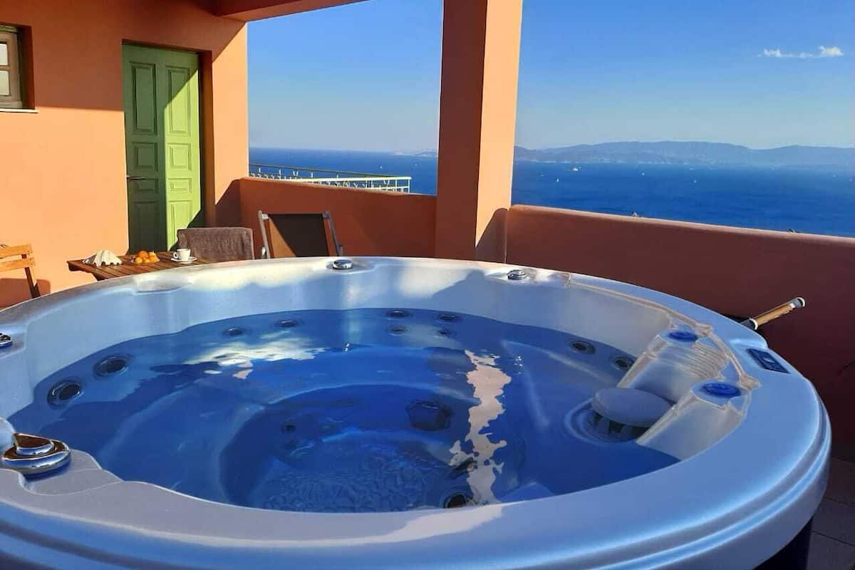 Un jacuzzi en un balcón con vista al mar y montañas a lo lejos.