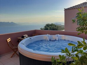 A hot tub on a balcony with a view of the sea and mountains.