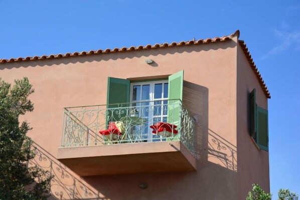 A building with a balcony featuring a metal railing and a window with green shutters.