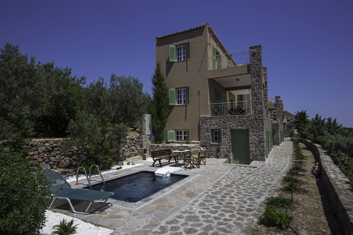 Un edificio de dos pisos de piedra con piscina, mobiliario exterior y un sendero de piedra.