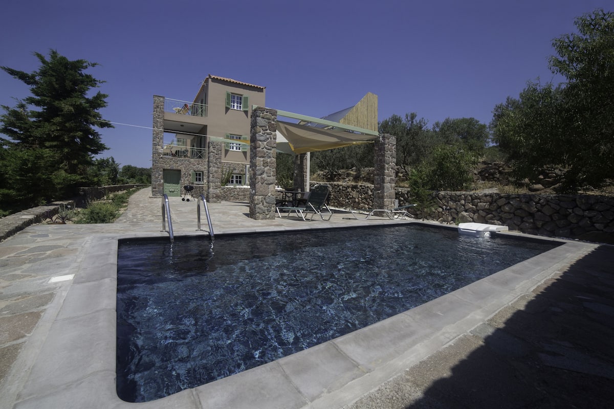 Una piscina con cubierta de piedra, un área de estar techada y un edificio con fachada de piedra al fondo.