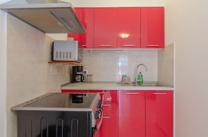 Une cuisine compacte avec des meubles rouges, un four encastré, un four à micro-ondes et une machine à café.