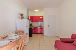 Un espace de vie compact comprenant un coin repas, une kitchenette et un canapé rouge.