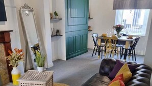 A living room with a dark leather sofa, a green door, and a dining area with a table and chairs. - Junctions Way by Tŷ SA -3 bed in Newport (Newport)