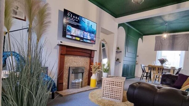 A living room with a fireplace, a television mounted on the wall, and a dining area visible through an archway. - Junctions Way by Tŷ SA -3 bed in Newport (Newport)