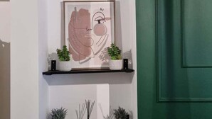A hallway with a green door, white walls, and a framed artwork above a shelf with potted plants. - Junctions Way by Tŷ SA -3 bed in Newport (Newport)