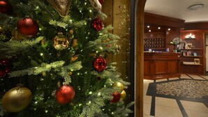 A Christmas tree with ornaments, a reception area with a counter, and a patterned rug. - Hotel Primula (Livigno)